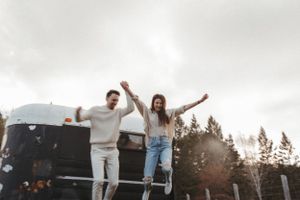 A joyful couple in casual wear celebrating on top of a dark surface with trees in background.