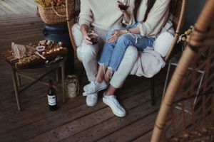Casual couple relaxing on wooden deck chairs with cozy blankets and drinks.