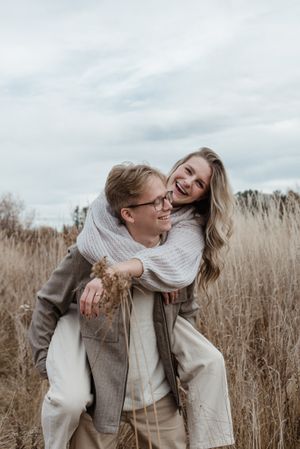 Couple shares joyful moment together while wearing warm sweaters in autumn field.