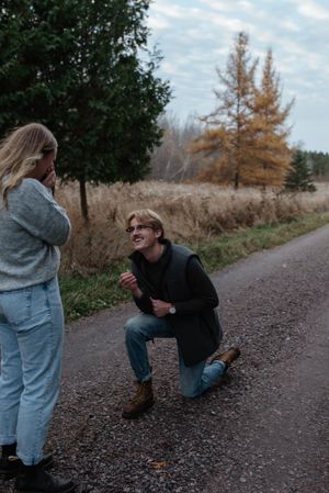 A surprise proposal moment captured on a country path with autumn trees in the background.