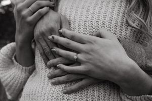 Close up of hands displaying an engagement ring on a knit sweater background.