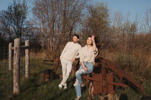A couple posing casually on rustic farm equipment in a natural outdoor setting.