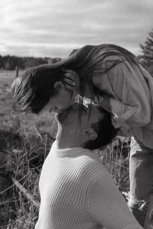 An intimate black and white portrait of a couple sharing a tender moment in a natural outdoor setting.