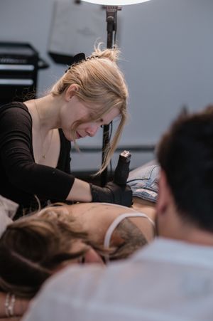 Close-up of tattoo artist working on client's arm in studio setting.