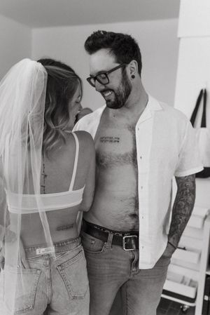 Couple in casual attire showing their matching tattoos in black and white photography.