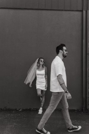 Artistic black and white shot of couple walking past brick wall.