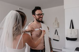Couple shares intimate moment during wedding preparation in bright indoor setting.