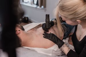Tattoo artist prepares to work on client in professional studio setting.