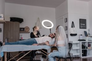 Professional tattoo session in progress with artists working on a client under ring light in a modern studio space.