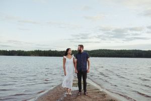 A couple walks hand in hand on a narrow pier extending into a serene lake.