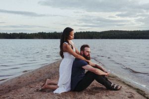 A couple sits together on a rocky shoreline overlooking a peaceful lake at dusk.