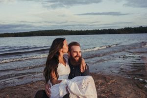 A couple shares a joyful moment while sitting on rocks by a lakeside during golden hour.