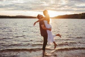 A romantic sunset moment at a lake with a joyful embrace and lifting pose against the golden light.