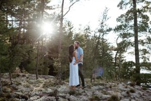 A romantic moment captured between a couple on a rocky cliff with sunlight streaming through pine trees.
