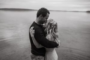 An intimate black and white portrait of a couple embracing by the water.