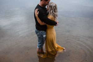 A couple standing in shallow water with a flowing yellow dress catching the breeze.