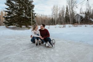 A couple sitting together on ice skates in a snowy winter landscape.