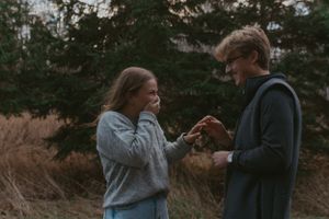 A romantic outdoor moment captured between two people surrounded by evergreen trees.