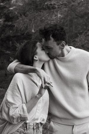 A romantic black and white photograph of a couple sharing an intimate kiss while wearing light-colored sweaters.