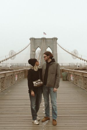 Couple sharing a moment on the iconic Brooklyn Bridge walkway on a foggy day.