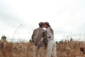Two people share an intimate moment while standing in a golden field at sunset.