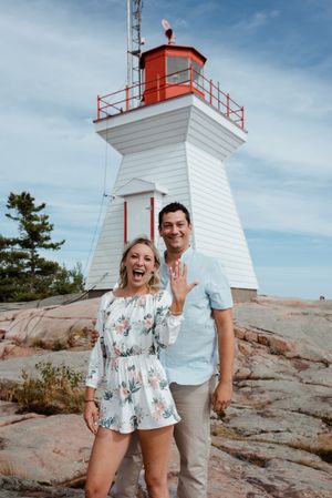A joyful celebration in front of a white lighthouse with red trim on rocky coastal cliffs.