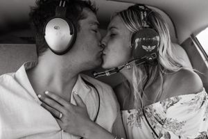Black and white photo of a couple sharing a kiss while wearing aviation headsets.