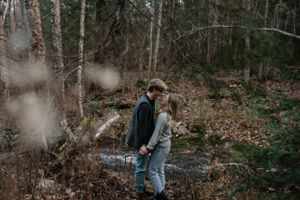 A couple explores a woodland trail together on a misty autumn day.