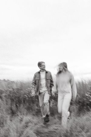 A blurred black and white photo of a couple walking through a field of tall grass.