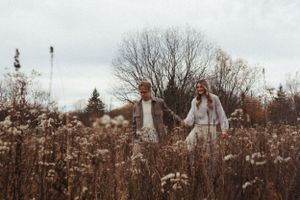 Couple holding hands while standing in a field of tall wild grass on an overcast day.
