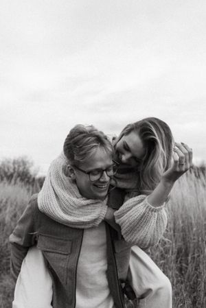 Black and white photo of couple sharing intimate moment in field of tall grass.