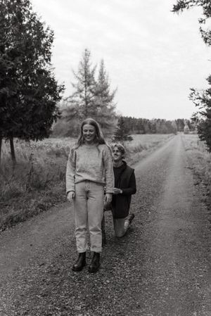 A candid black and white photo of two people on a rural dirt road surrounded by trees.
