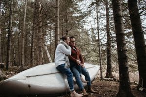 A couple sitting together on an overturned canoe in a pine forest.