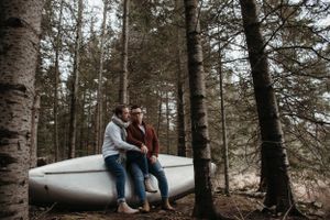 A couple sharing a tender moment while sitting on a canoe in a wooded setting.