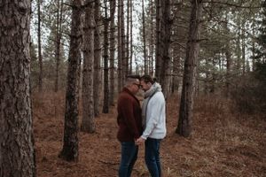 A couple sharing an intimate moment among tall pine trees in a forest.