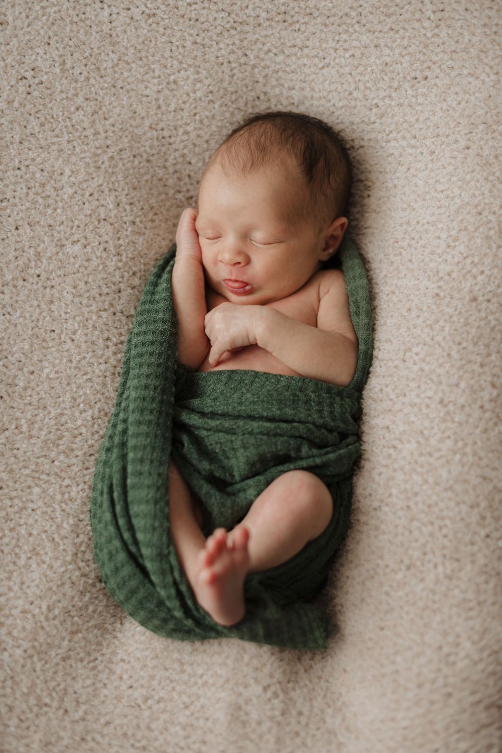 Newborn baby peacefully sleeping on a soft beige blanket, wrapped in a green swaddle.