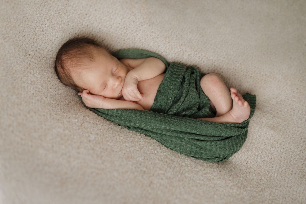 Newborn baby peacefully sleeping on a soft beige blanket, wrapped in a green swaddle.