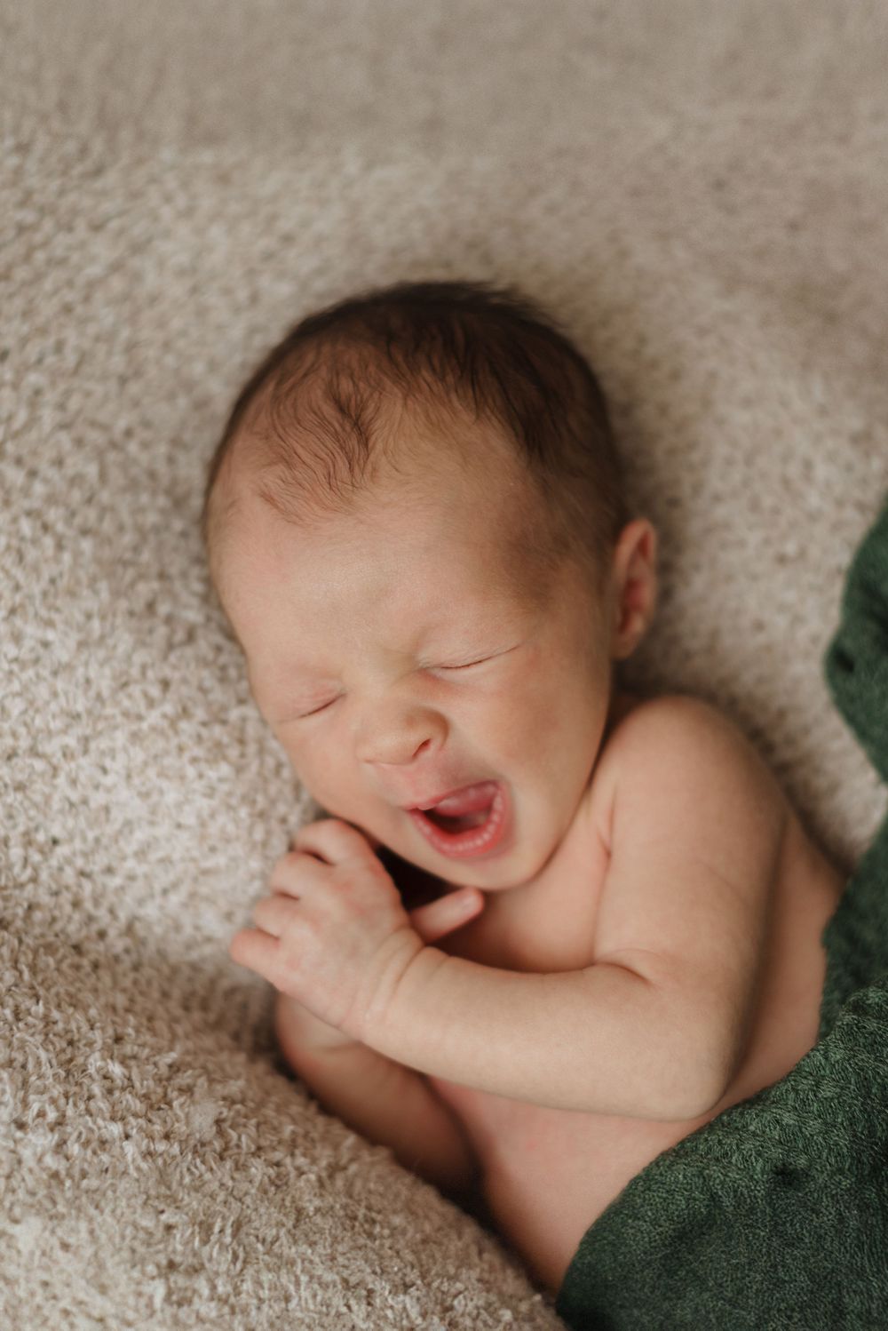 Newborn baby peacefully sleeping on a soft beige blanket, wrapped in a green swaddle.