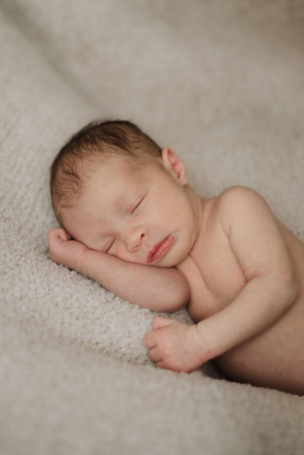Newborn baby peacefully sleeping on a soft beige blanket, wrapped in a white swaddle.