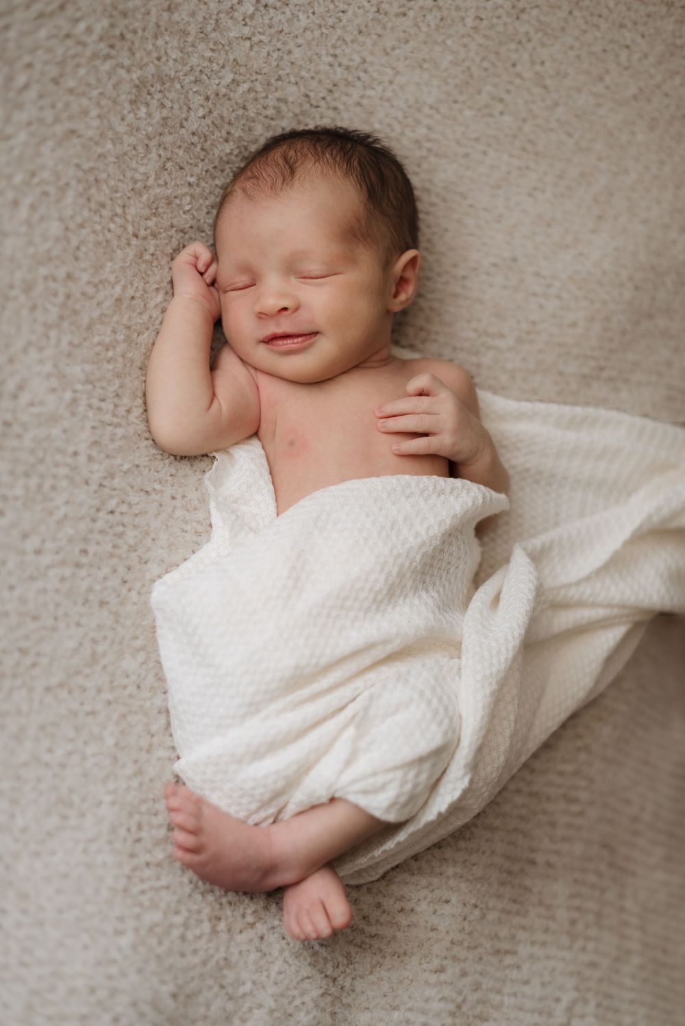 Newborn baby peacefully sleeping on a soft beige blanket, wrapped in a white swaddle.