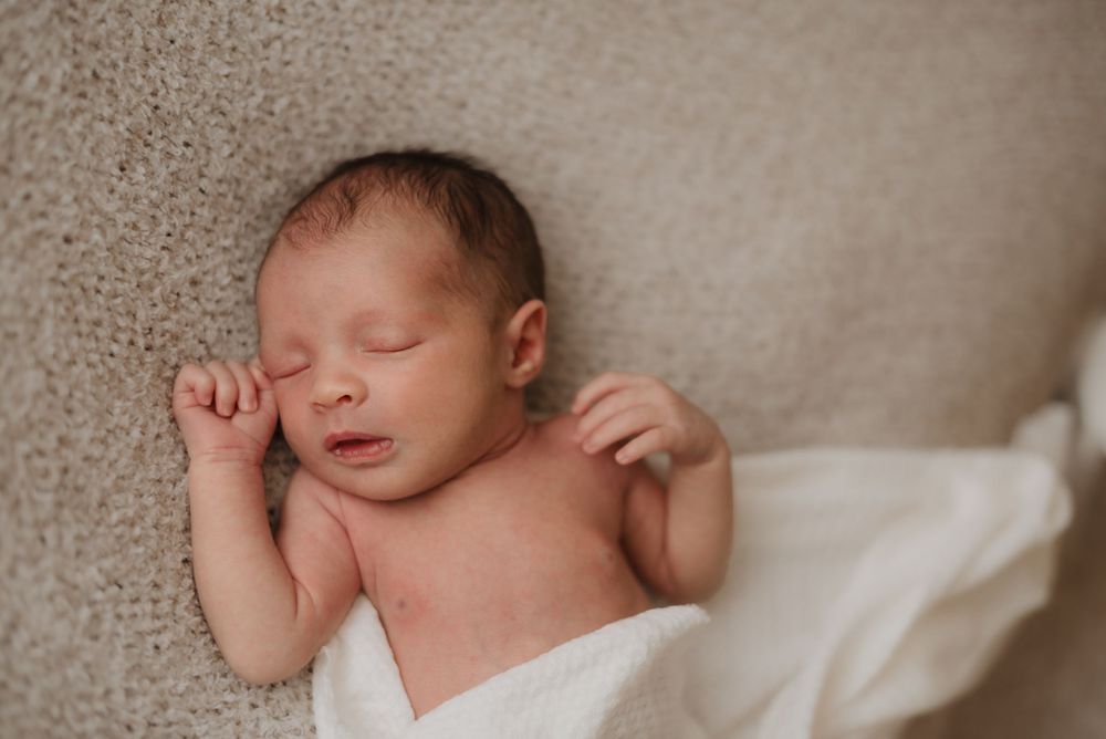 Newborn baby peacefully sleeping on a soft beige blanket, wrapped in a white swaddle.