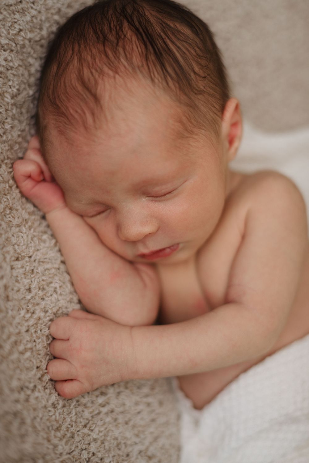 Newborn baby peacefully sleeping on a soft beige blanket, wrapped in a white swaddle.