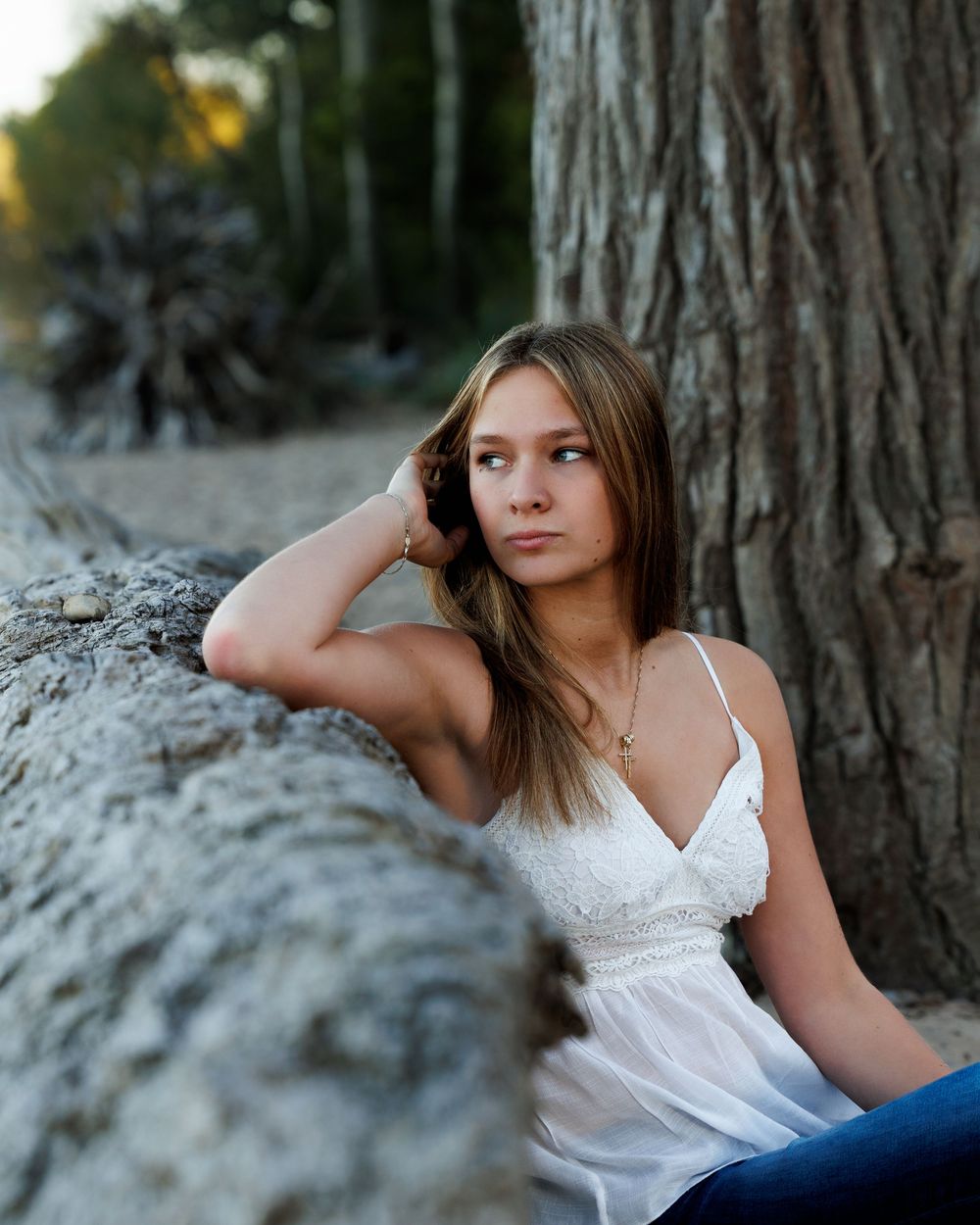 Casual outdoor photoshoot with someone reclining against a large tree trunk in natural lighting.