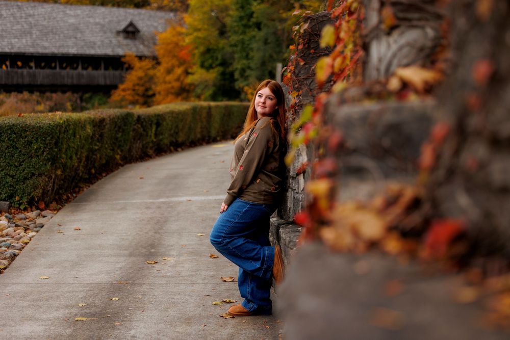 A person in blue jeans walks along a stone path surrounded by vibrant autumn foliage and trees.