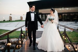 A bride and groom walk hand in hand down a candlelit path at an outdoor evening wedding ceremony.