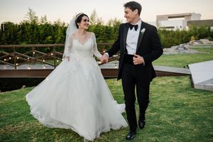 Newlyweds walk together on manicured grounds during their outdoor wedding photoshoot at sunset.