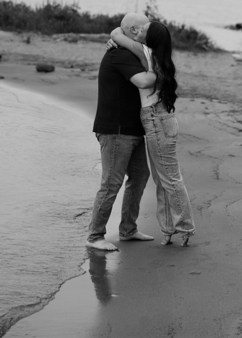 Black and white photo of feet standing in beach surf.