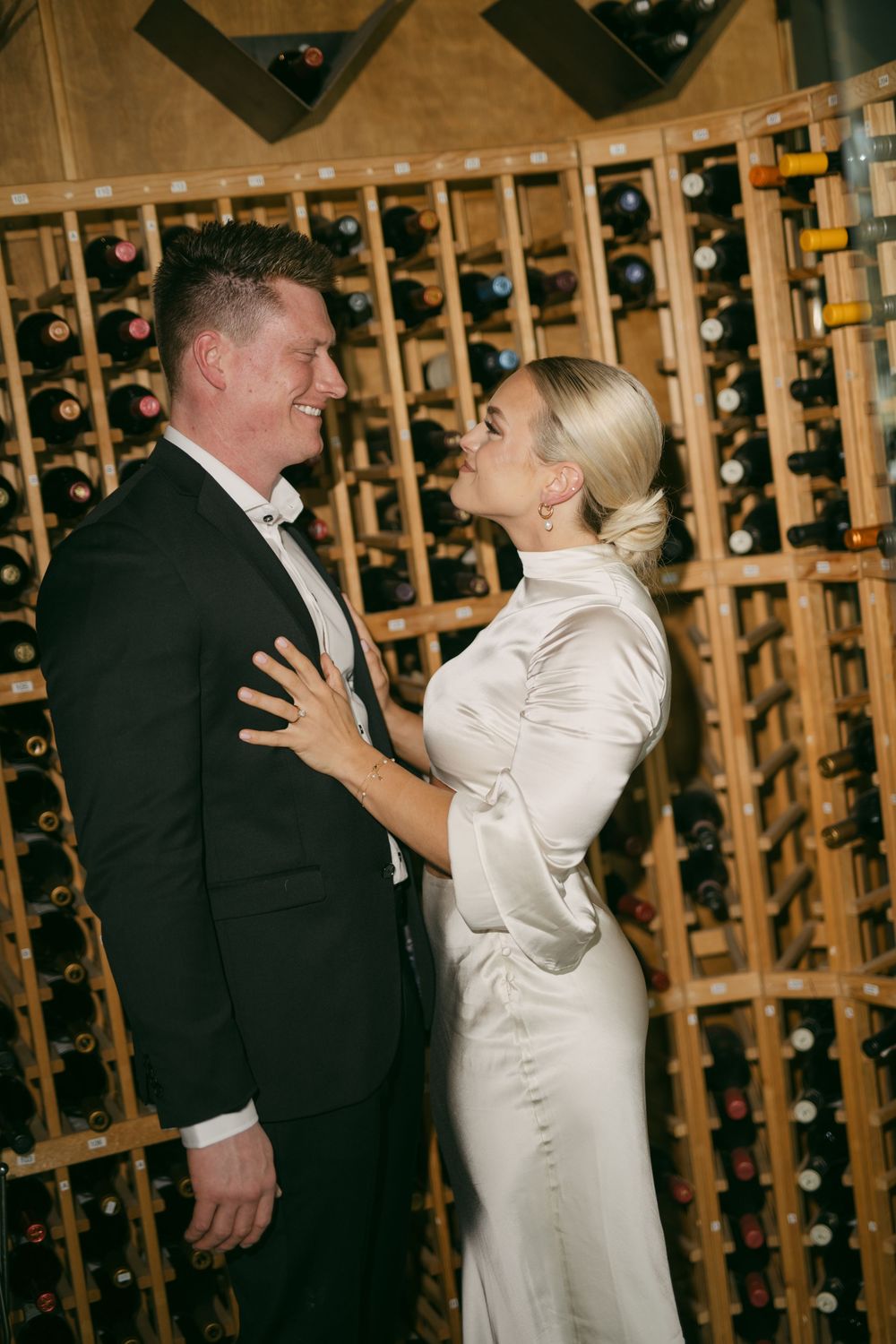 Elegant couple dancing and laughing in wine cellar with wooden racks.