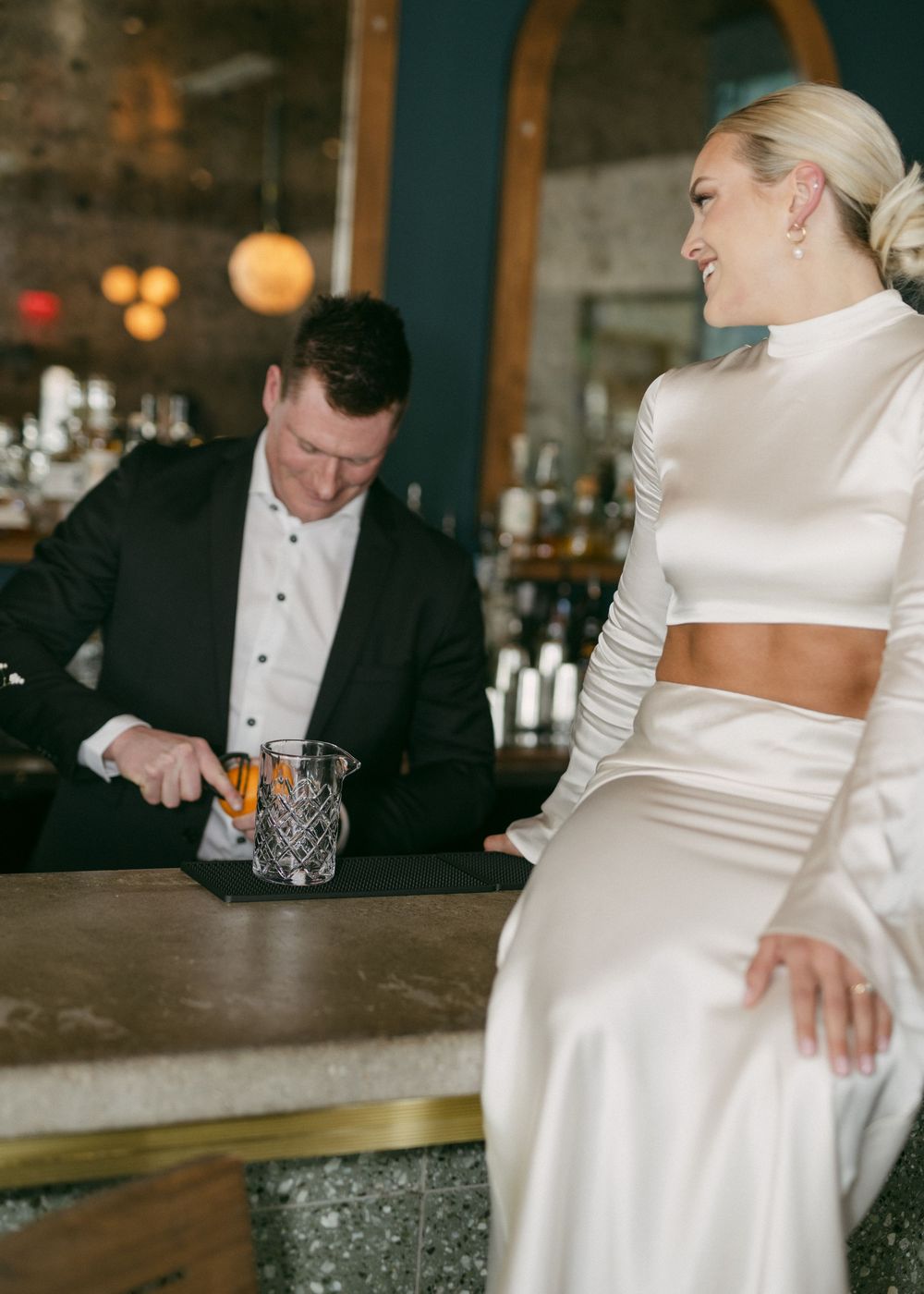 Bride in white satin dress and groom sharing intimate moment at bar.