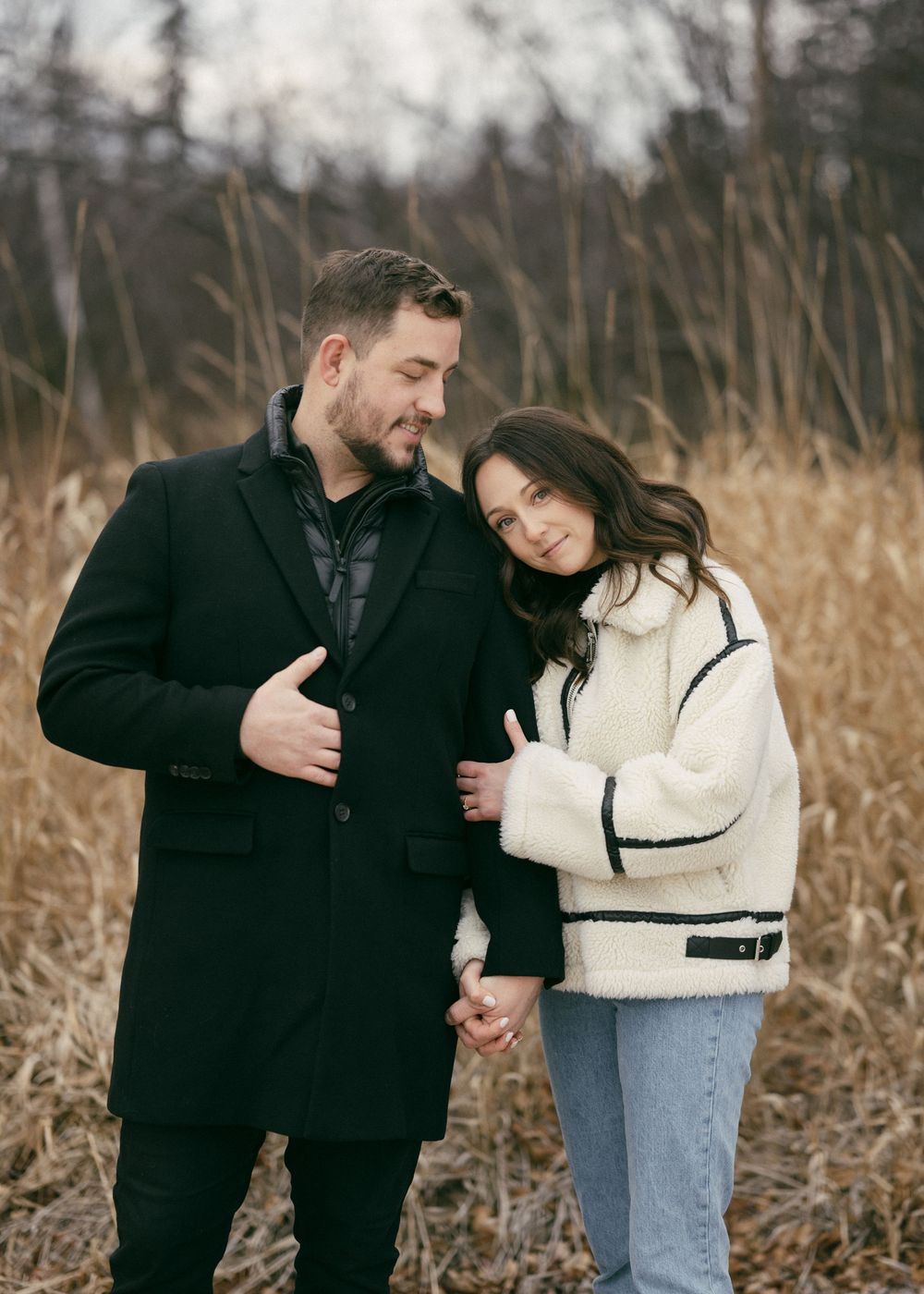 Romantic couple embracing in tall autumn grass during outdoor photoshoot.